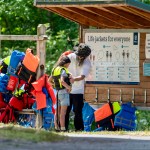 An adult helps a child into a life jacket in front of a free life jacket station at a Metro Park. That is one of the top water safety tips.